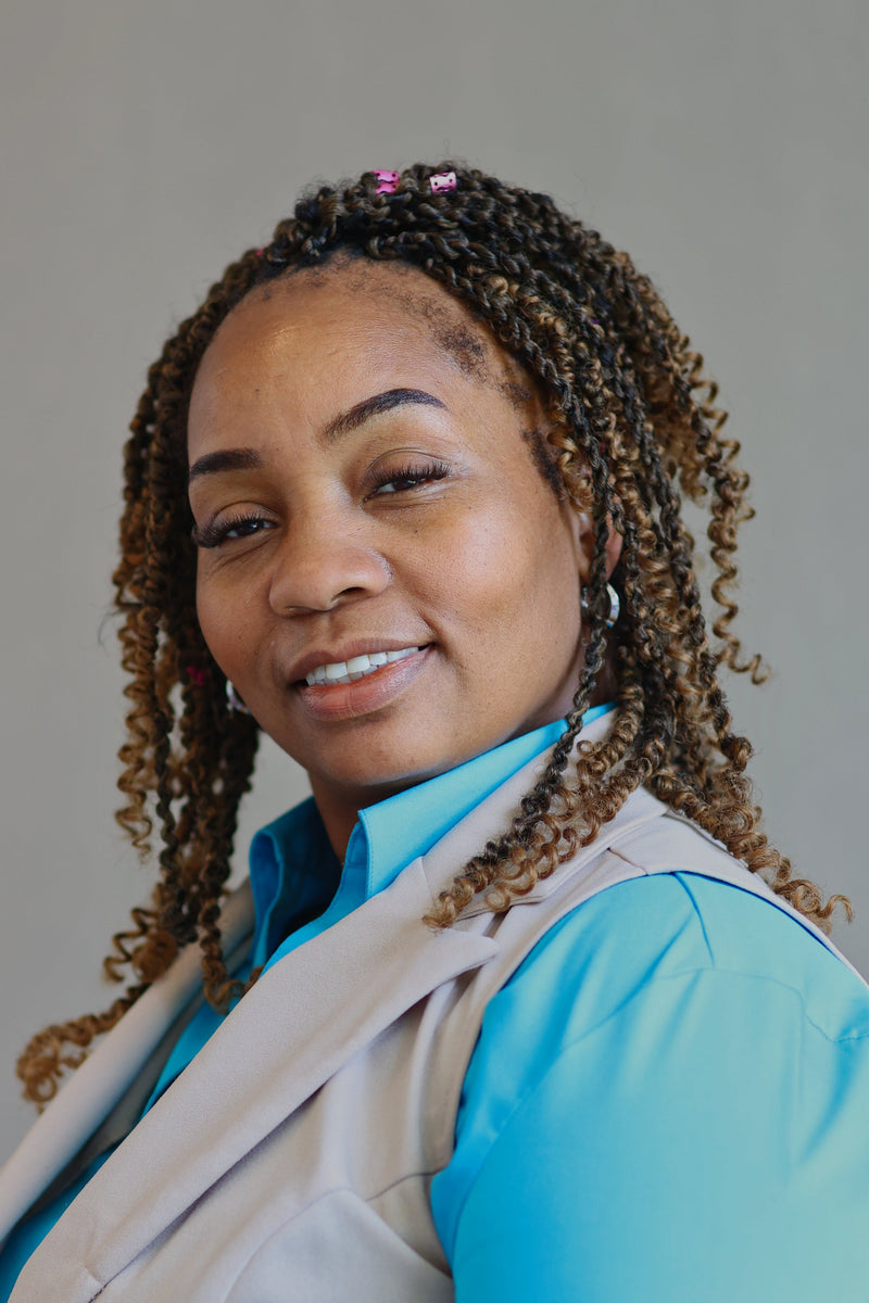 Woman wearing a blue shirt and beige vest against a gray background